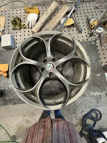 Silver five-spoke Alfa Romeo alloy wheel on the shop workbench before crack repair