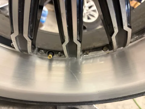 Rear barrel, flange and valve area of a cracked multi-spoke wheel before repair, with an old JB Weld patch