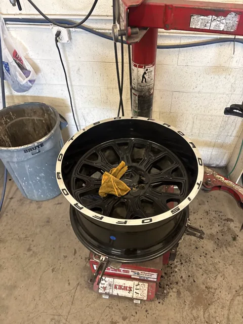 Front face of a black wheel with curb rash work in progress around the lip