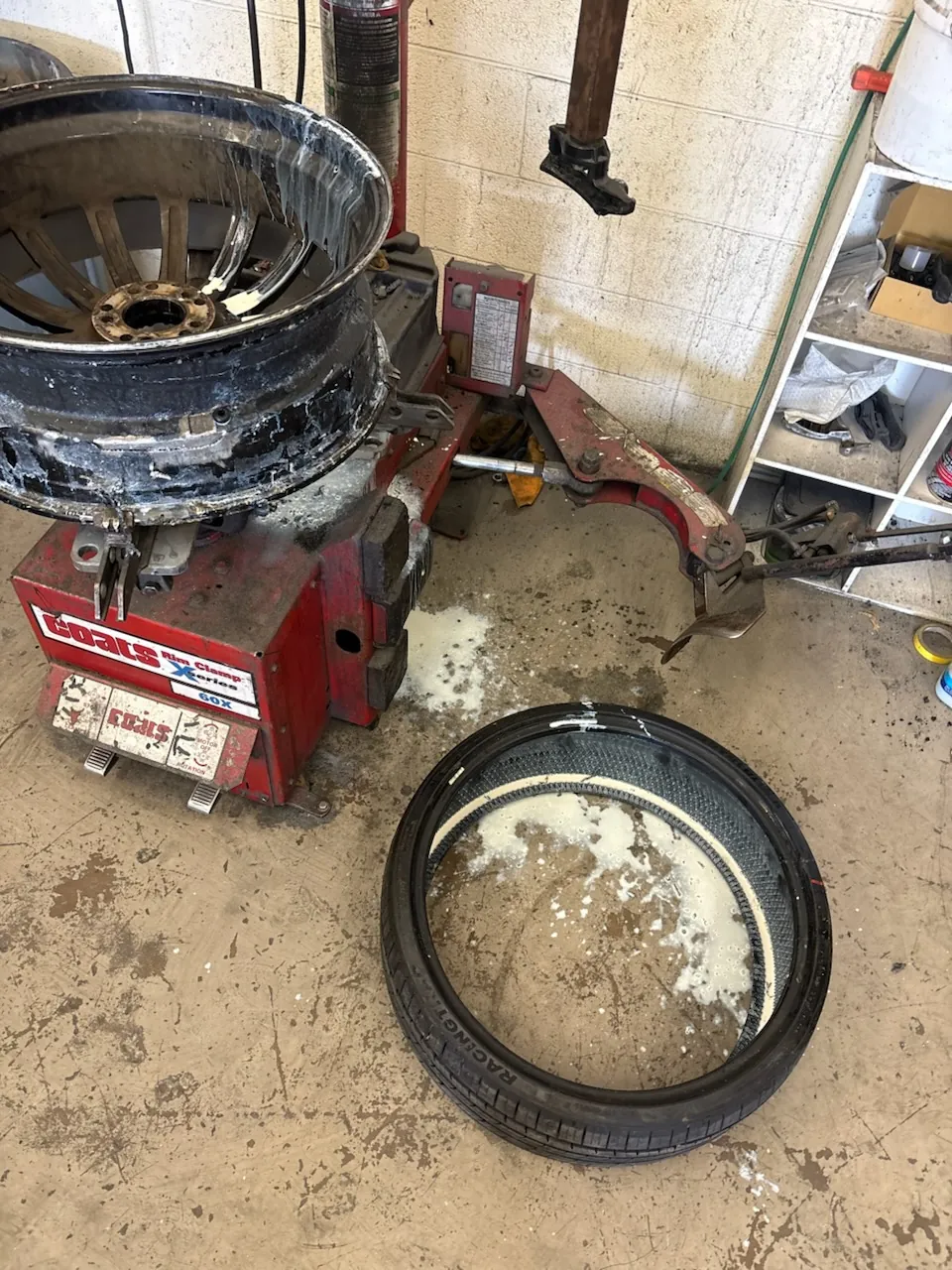 A wheel on the red Coats tire changer in the AZ Rim Repair shop, its barrel smeared with white tire sealant, with the dismounted low-profile tire on the floor beside it holding a pool of the same sealant